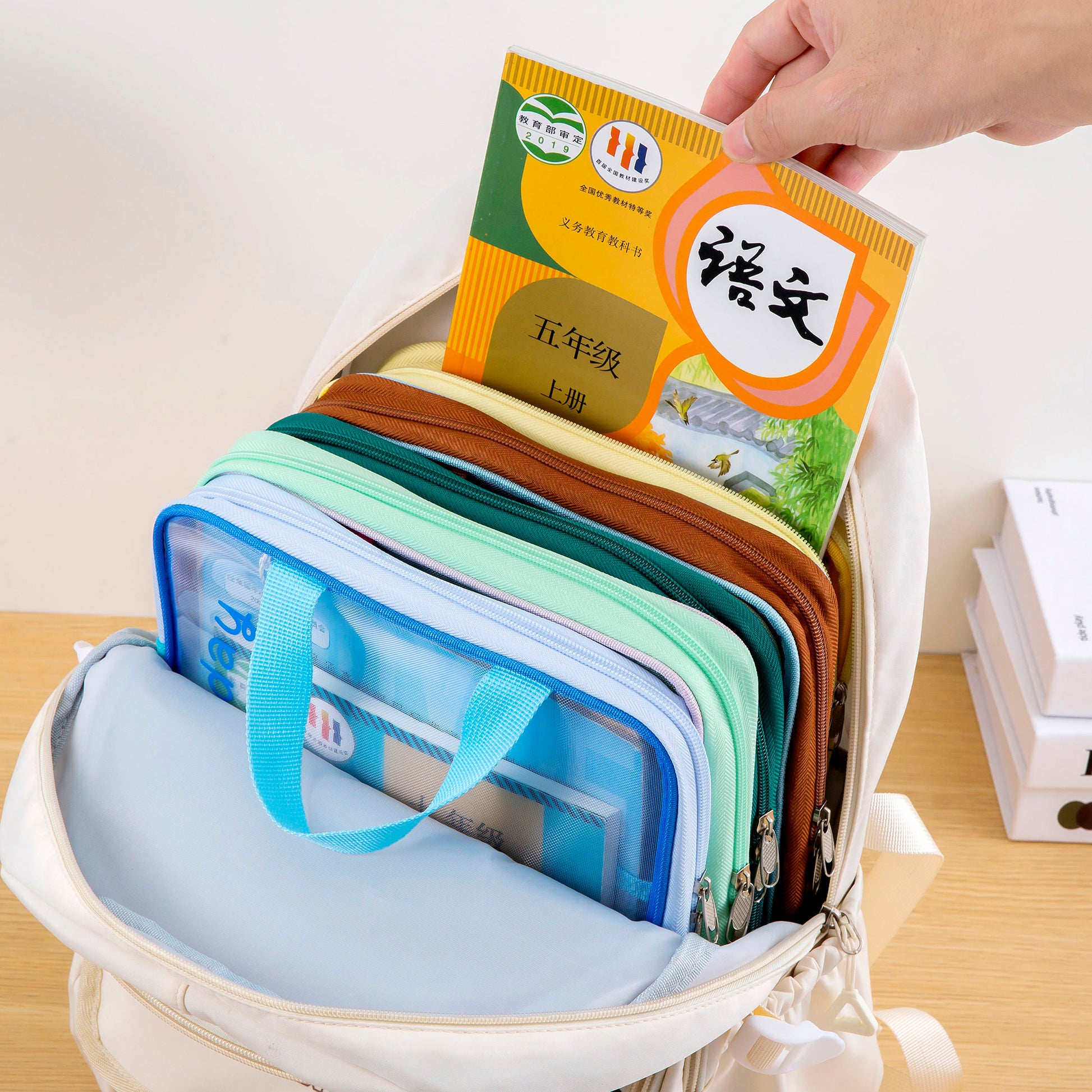 A hand demonstrating the convenient L-shaped vertical opening of the subject organizer bag to retrieve a textbook
