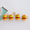 Four cute silicone hamburger keychain pouches with different animal toppers lined up neatly on a clean white surface next to a teal card