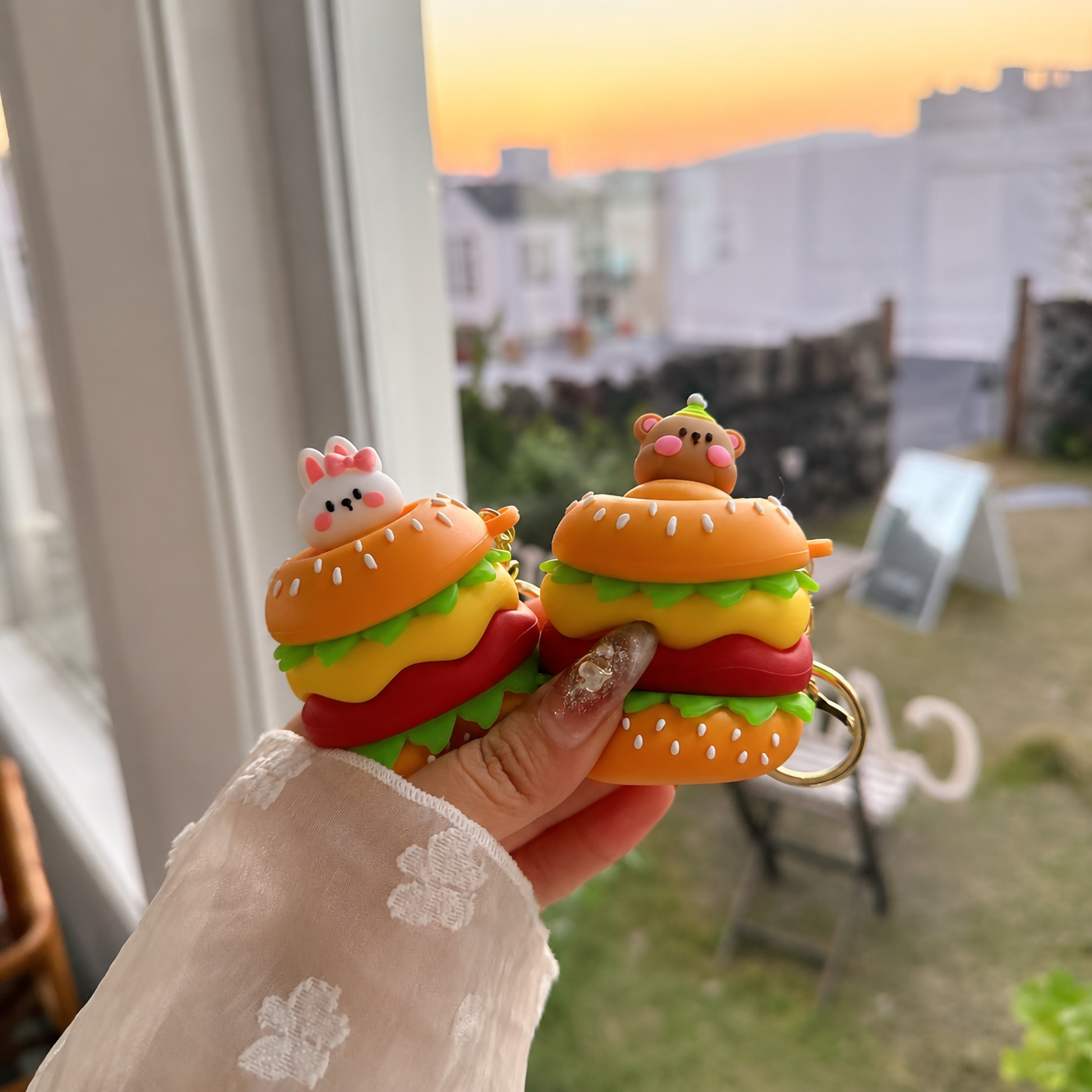 A row of vibrant, multi-layered 3D burger silicone charms with attached gold metal keyrings, highlighting the textured design and playful animal characters