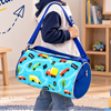 A young boy wearing a navy and white hoodie, jeans, and sneakers is shown in a bright children's room, carrying a light blue cylindrical duffel bag with a multicolor road-pattern print and blue straps. The image includes the text 'Small Bag Big Adventures' and is decorated with toys, books, and a teddy bear.