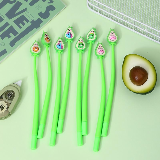 A collection of green barrel avocado shake gel pens displayed next to an open notebook and a fresh half-avocado on a light green background
