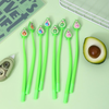A collection of green barrel avocado shake gel pens displayed next to an open notebook and a fresh half-avocado on a light green background