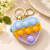 Close-up of a mini heart-shaped multi colored  pop it silicon pouch with a gold metal keyring attachment.