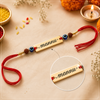 Close-up view of the gold nameplate reading "mannu" flanked by blue evil eye beads and white-gold beads on a teal and cream traditional setup.