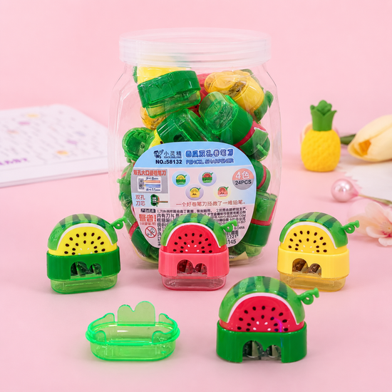 Cute watermelon shaped dual hole pencil sharpeners with transparent shavings collectors on a reflective desk.