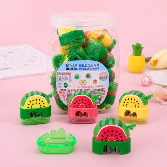 Cute watermelon shaped dual hole pencil sharpeners with transparent shavings collectors on a reflective desk.