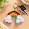 An overhead shot of the handmade rainbow bag charm resting on a clean white tabletop surface with Keys