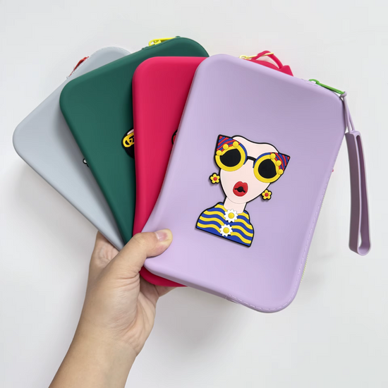 Four colorful silicone travel pouches (forest green, grey, purple, and pink) stacked vertically, each featuring a unique 3D fashion character design.