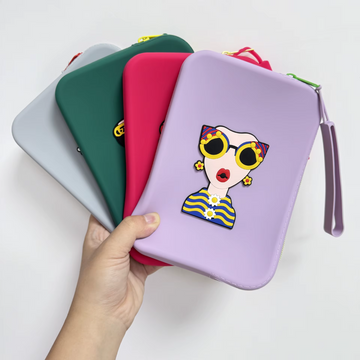Four colorful silicone travel pouches (forest green, grey, purple, and pink) stacked vertically, each featuring a unique 3D fashion character design.