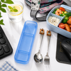 A lifestyle setting showing a mirror-polished stainless steel fork and spoon set topped with 3D cartoon bear handles next to an open Purple plastic travel case on a white desk
