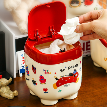 Small cream desktop trash can with red pop-up lid and cute animal stickers.