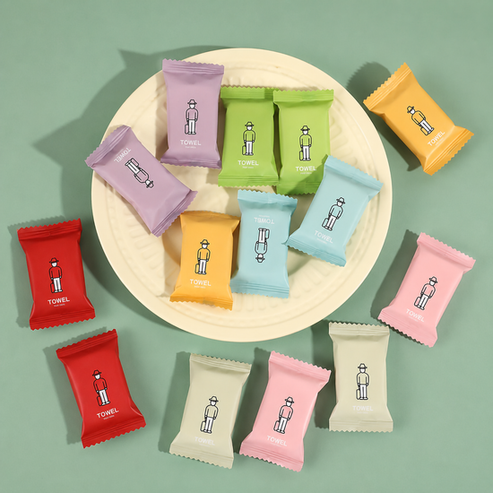 A high-angle close-up view showcasing multiple colorful individual candy-style compressed travel towel packages scattered on a beige surface
