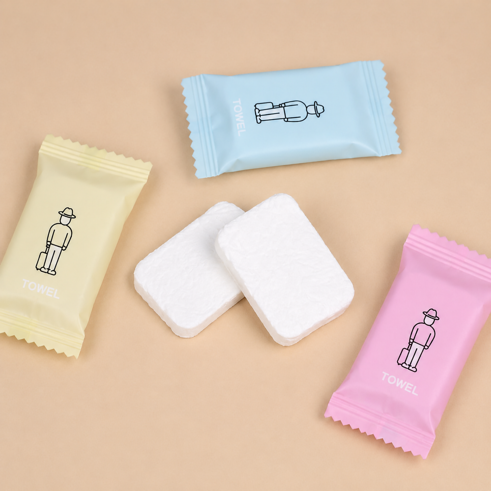 wo rectangular white compressed coin towel tablets set on a plain table next to their light blue and pink individual travel wrappers